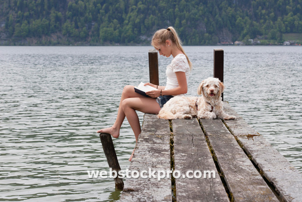 Austria, Teenage girl reading book beside dog on jetty