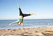 Young Woman In Fitness Clothing Turning Cartwheel On Beach Photo (mon214012)