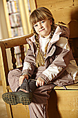 Young Girl Sitting On Wooden Seat Putting On Warm Outdoor Clothes And Boots Photo (MON290007)